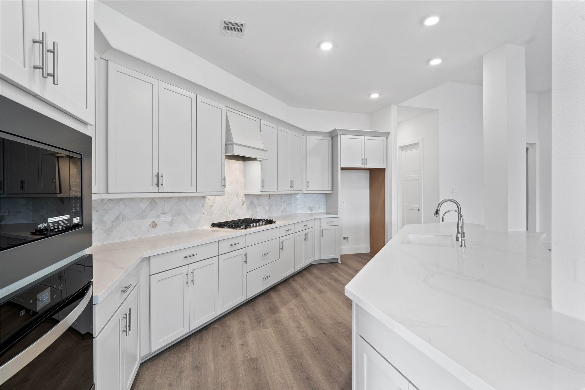 A sleek, built-in oven and microwave stack is seamlessly integrated into the cabinetry, complemented by a matching ventilation hood over the gas cooktop.