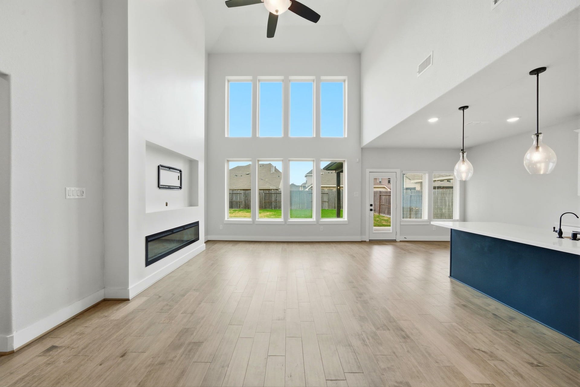 8815 Morning Glow Drive, Missouri City, TX 77459 Spacious, modern living area with high ceilings and large windows for abundant natural light. Features a sleek fireplace, open layout, and stylish kitchen island with pendant lighting. Perfect for entertaining and family living.