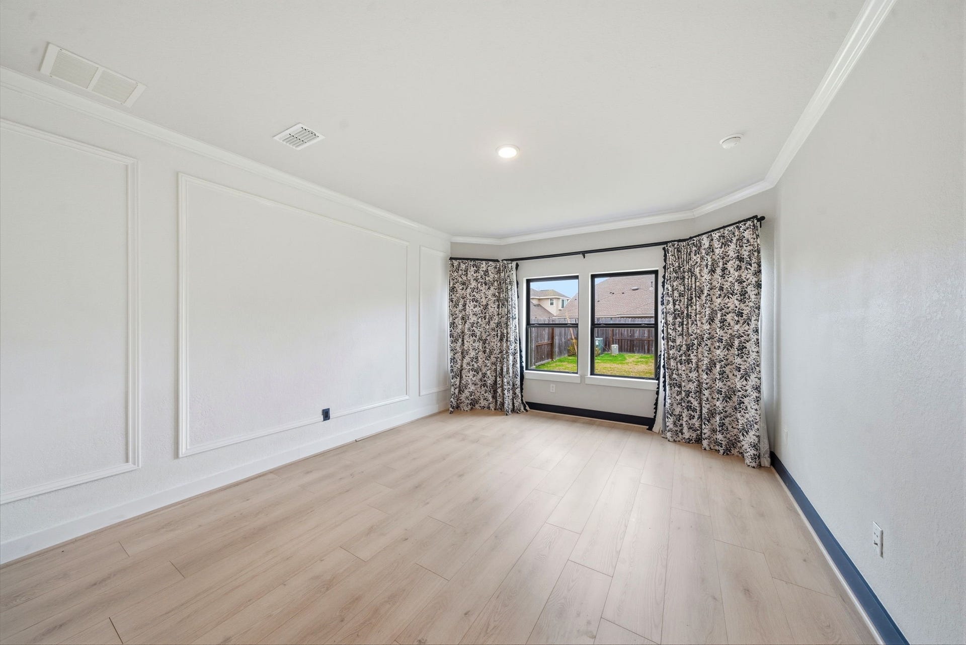 8815 Morning Glow Drive, Missouri City, TX 77459 Bright, spacious room with light wood flooring, large windows with patterned curtains, and elegant wall paneling. Ideal for a cozy living area or home office.