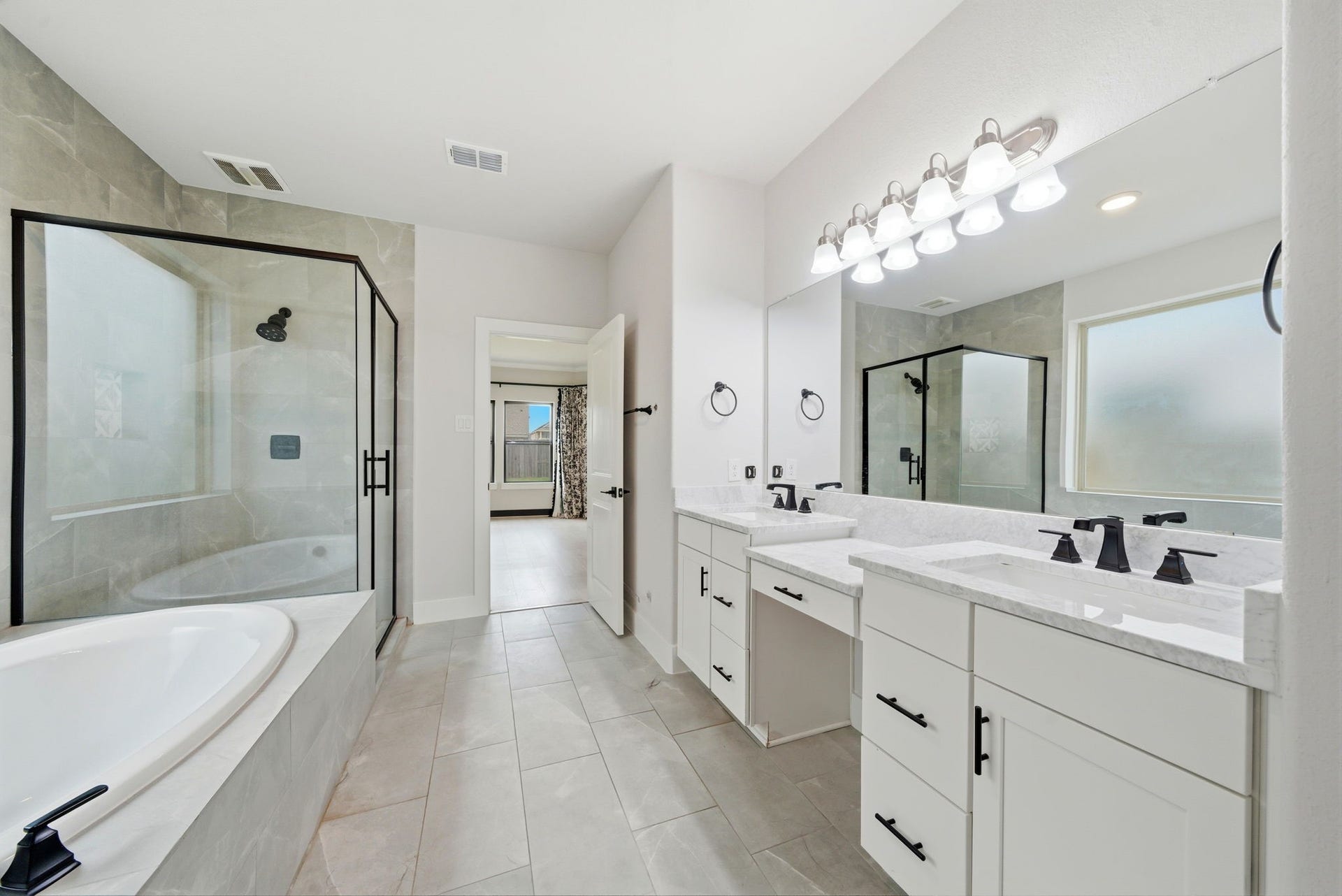 8815 Morning Glow Drive, Missouri City, TX 77459 This is a modern, spacious bathroom featuring a glass-enclosed shower, a separate bathtub, dual sinks with ample counter space, and elegant fixtures. The large mirror and bright lighting enhance the room's airy feel.