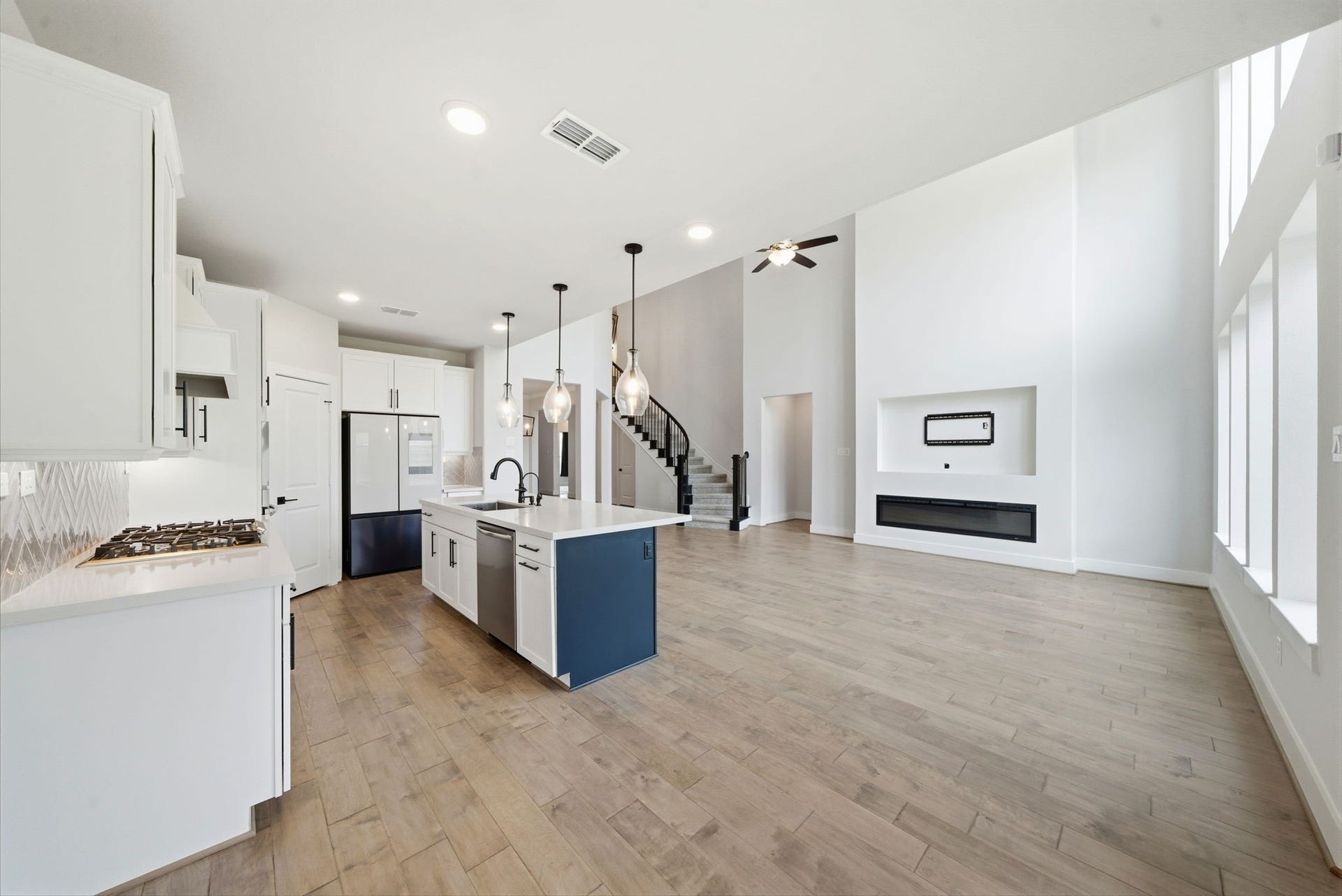 8815 Morning Glow Drive, Missouri City, TX 77459 This photo showcases a spacious, open-concept kitchen and living area with high ceilings and large windows. The kitchen features modern appliances, a central island with pendant lighting, and sleek cabinetry. The living area includes a stylish built-in wall feature and contemporary staircase.
