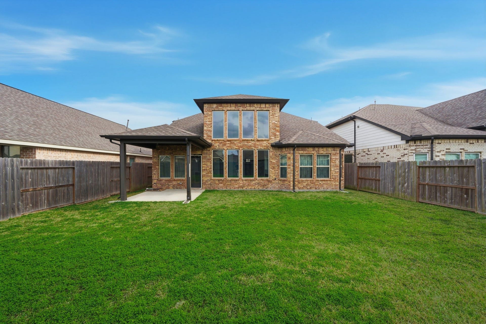 8815 Morning Glow Drive, Missouri City, TX 77459 This photo features a spacious backyard with a well-maintained lawn, surrounded by wooden fencing. The house is a two-story brick structure with large windows, offering a covered patio area perfect for outdoor relaxation or gatherings.