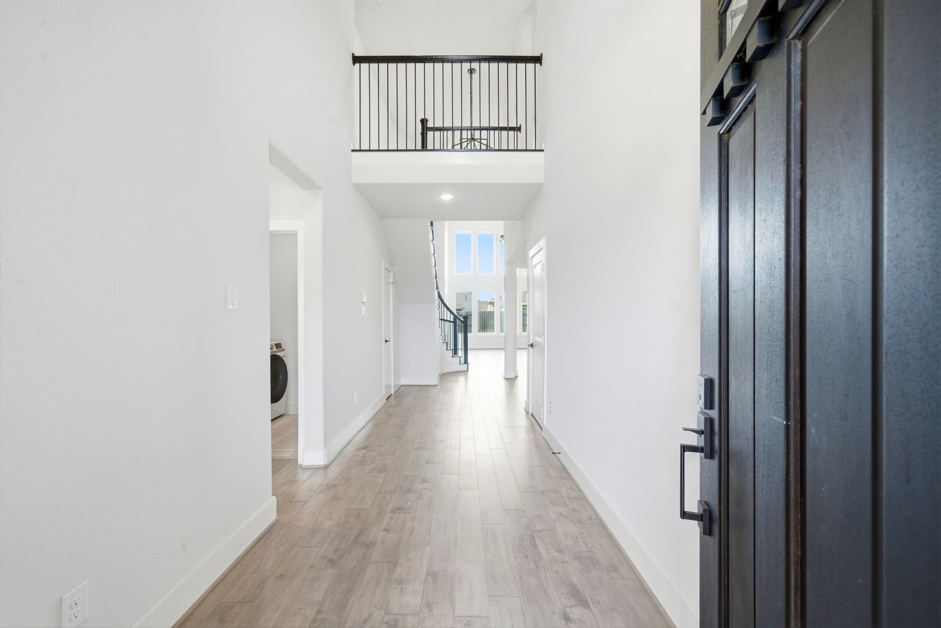 8815 Morning Glow Drive, Missouri City, TX 77459 This photo showcases a bright, open foyer with a high ceiling and a view of a modern staircase. The space features light wood flooring and leads into a well-lit living area with large windows, creating an inviting entrance.