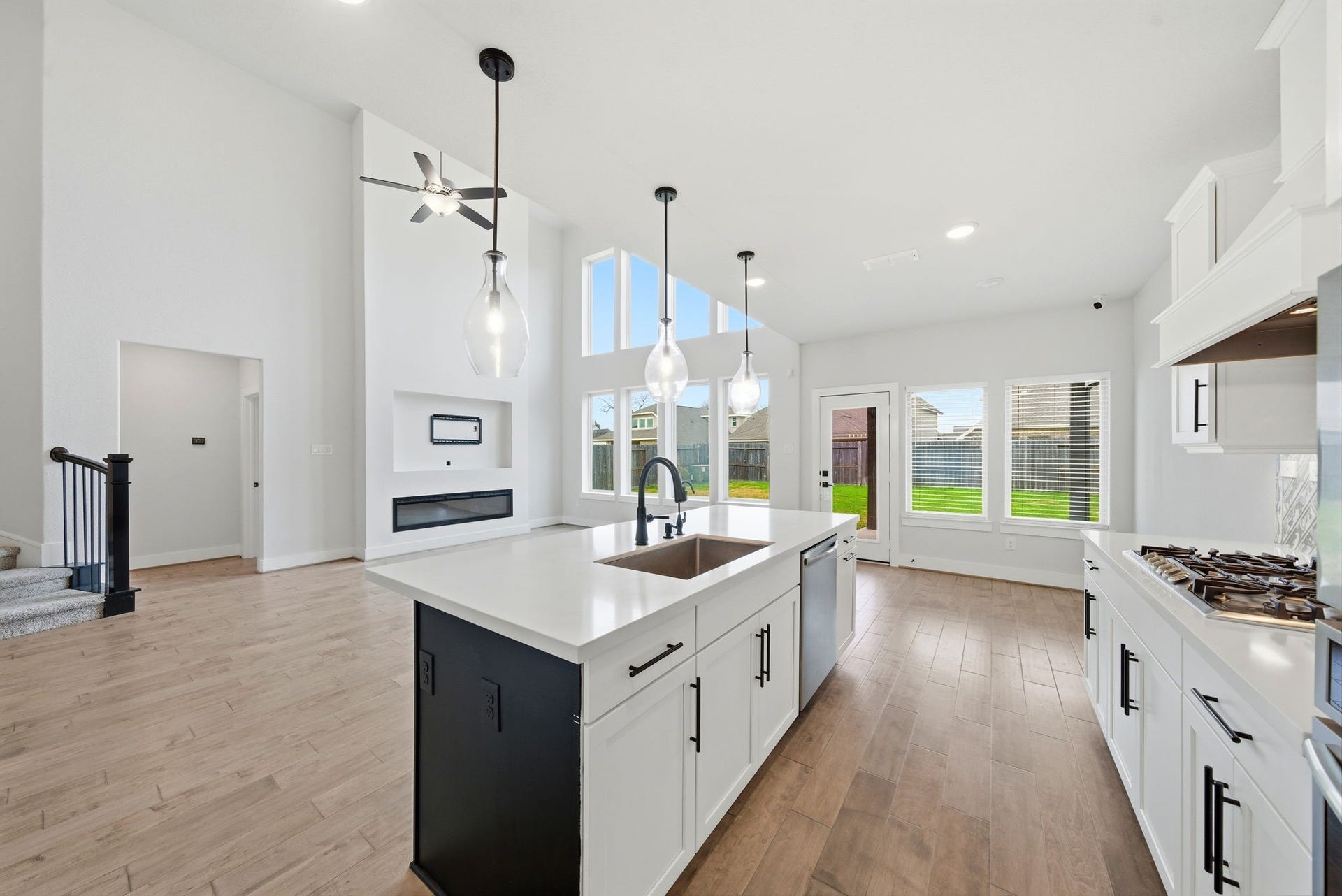 8815 Morning Glow Drive, Missouri City, TX 77459 This modern open-concept living space features high ceilings and abundant natural light. The kitchen boasts sleek white cabinetry, a central island with a sink, and stainless steel appliances. Large windows offer views of the backyard, and the area seamlessly connects to the living room with a contemporary fireplace.