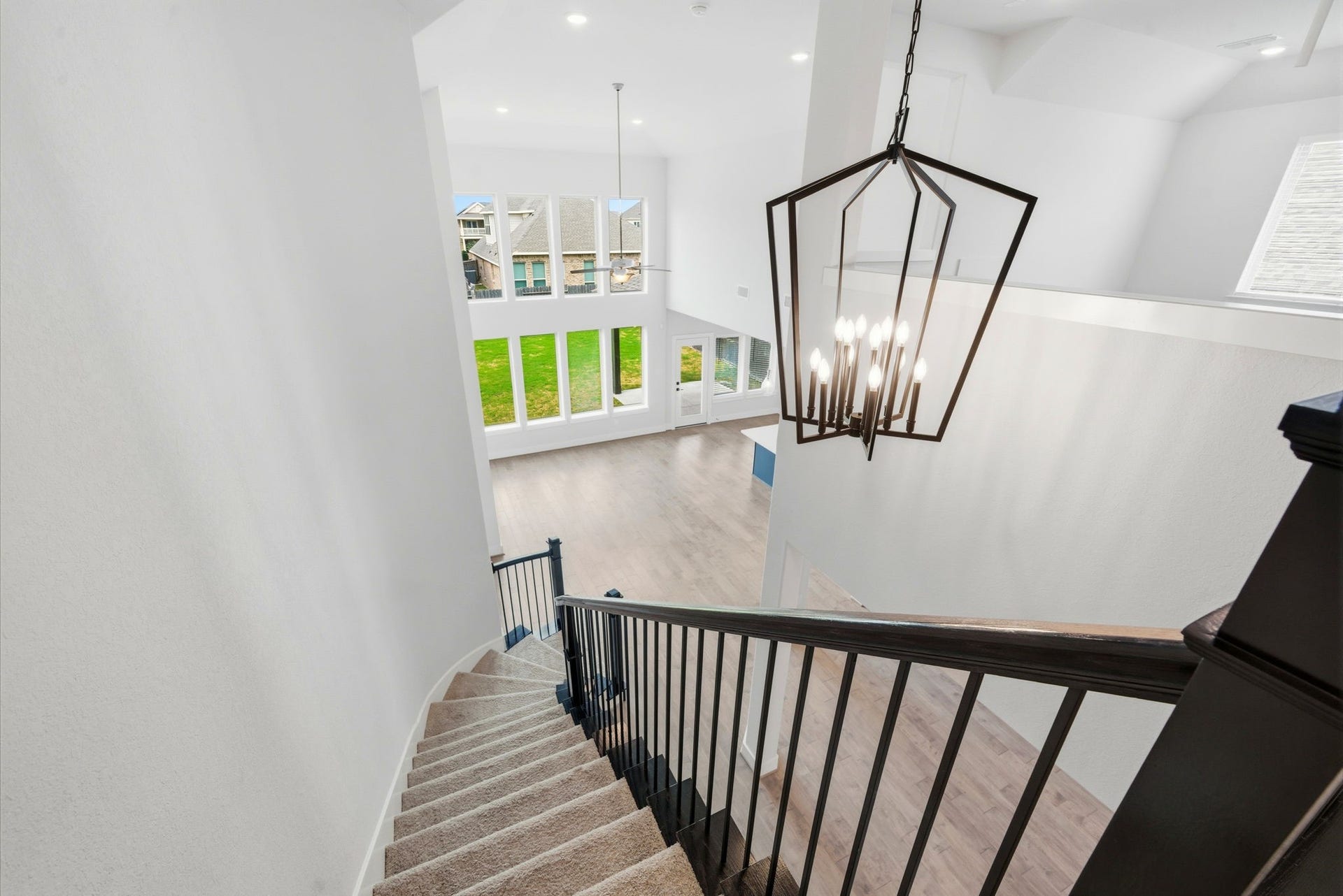 8815 Morning Glow Drive, Missouri City, TX 77459 This photo showcases a bright, modern home with a view from the top of a carpeted staircase. The space features high ceilings, a large geometric chandelier, and expansive windows that let in plenty of natural light, offering a view of the outdoors and creating an open, airy atmosphere.