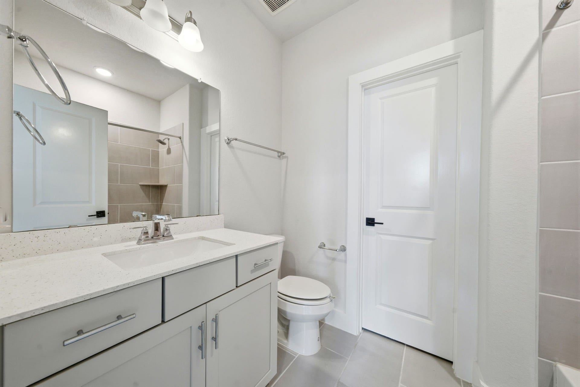 8815 Morning Glow Drive, Missouri City, TX 77459 This modern bathroom features a sleek vanity with ample storage, a large mirror with stylish lighting, a clean white countertop, a toilet, and a spacious shower with neutral tiling.