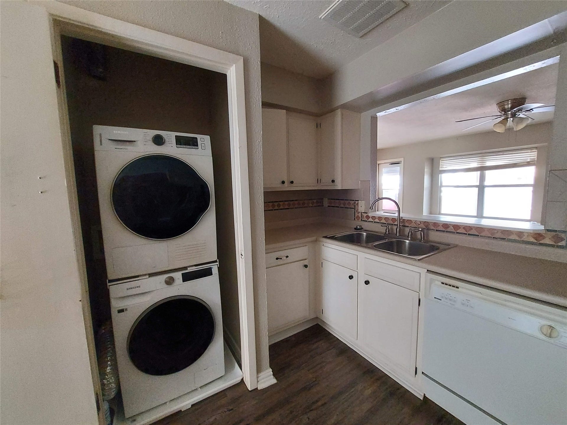 3878 Laura Leigh Drive, Friendswood, TX 77546 Charming kitchen with convenient stacked washer and dryer, ample cabinetry, dual sink, and a dishwasher, all accented by a decorative backsplash.