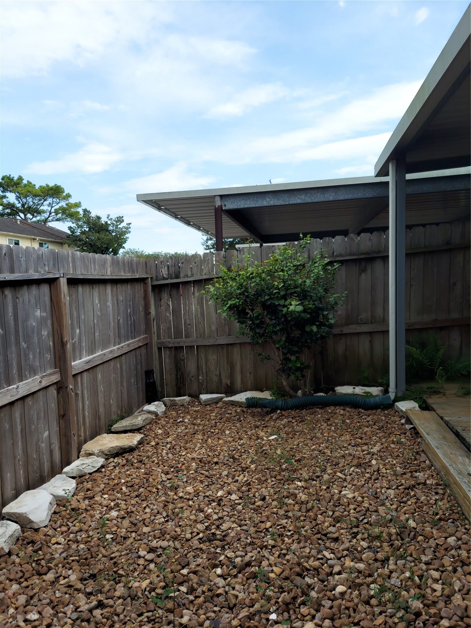 3878 Laura Leigh Drive, Friendswood, TX 77546 Charming backyard space with a wooden fence, covered patio, and low-maintenance gravel landscaping.