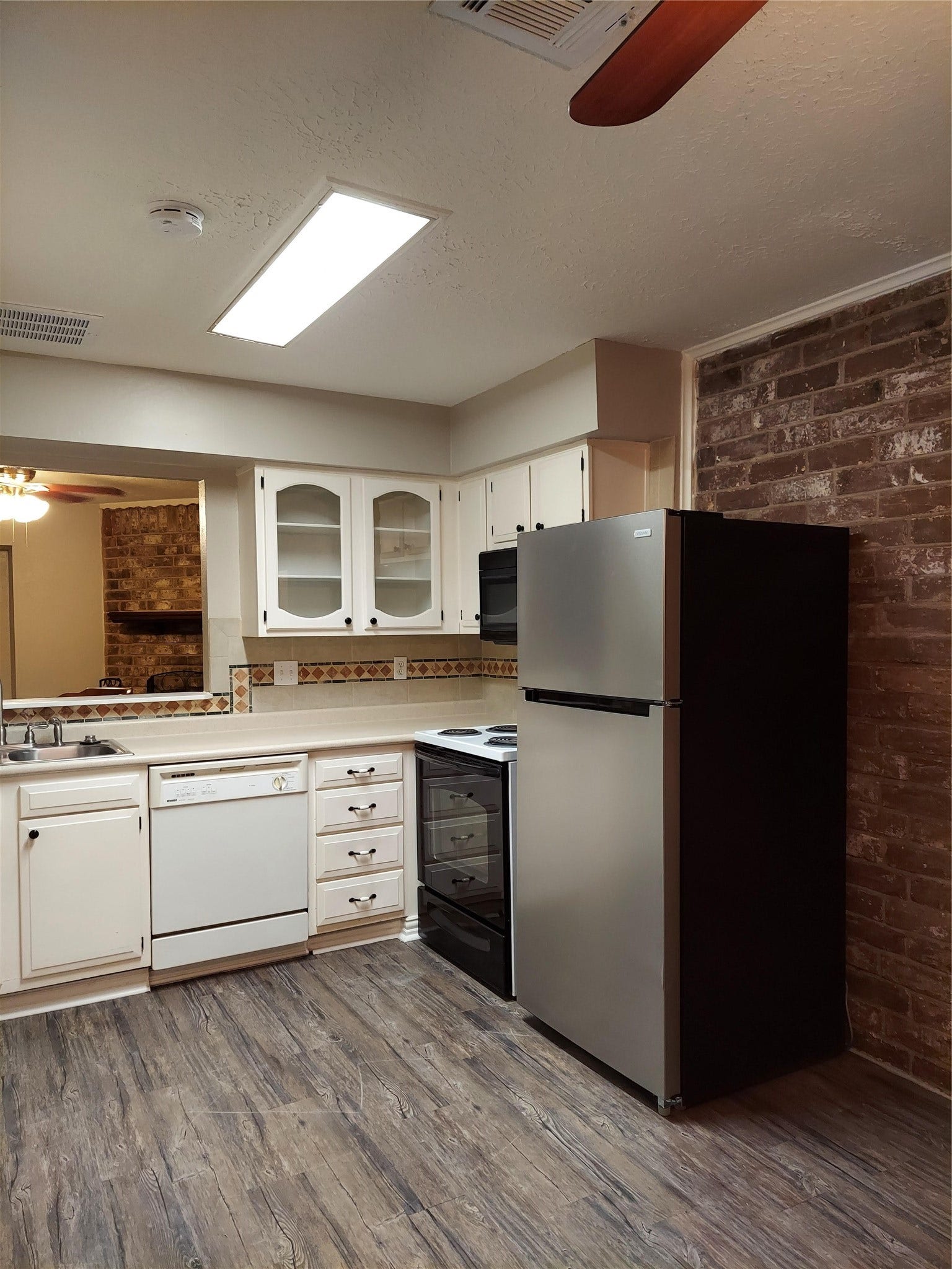 3878 Laura Leigh Drive, Friendswood, TX 77546 Charming kitchen with rustic brick accents, modern stainless steel fridge, and ample cabinetry, complemented by sleek wood-look flooring and a cozy pass-through to the living area.