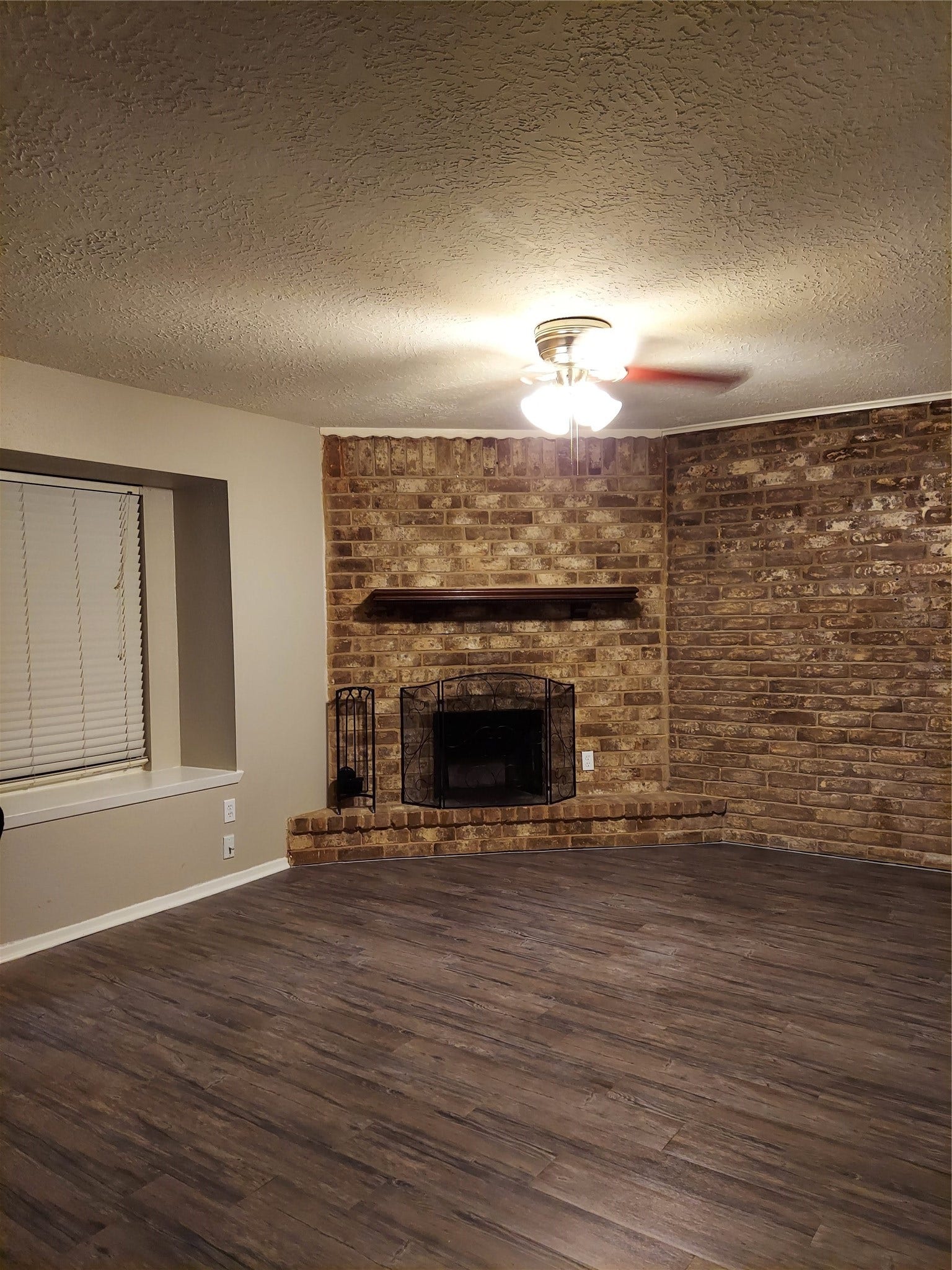 3878 Laura Leigh Drive, Friendswood, TX 77546 Cozy living room featuring a charming brick fireplace, complemented by sleek wood flooring and a ceiling fan for comfort.