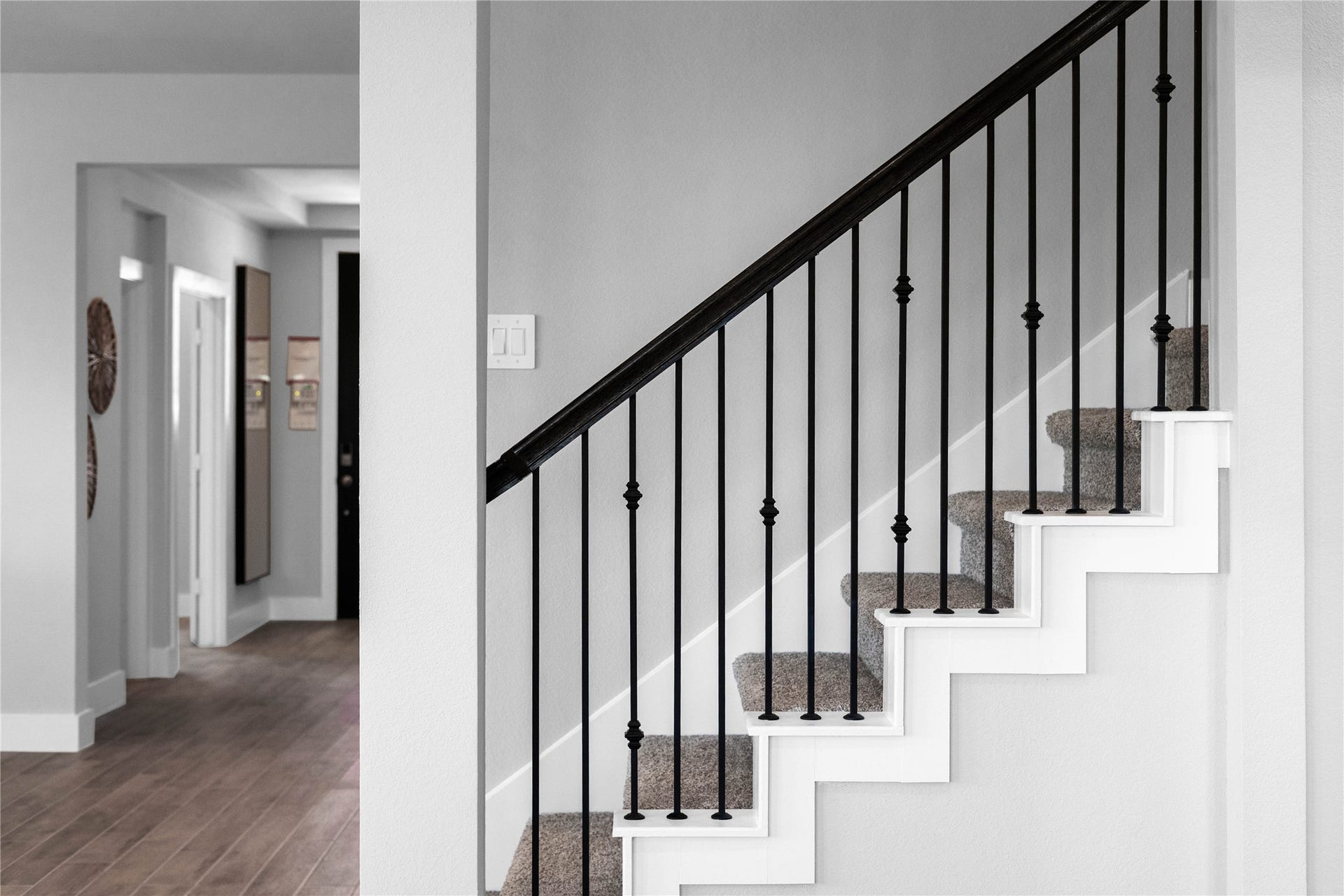 19608 Montgomery Ridge Way, Montgomery, TX 77316 An elegant staircase featuring a modern mix of materials, including sleek black wrought iron balusters with decorative knuckle accents. The clean white risers and plush neutral carpeting create a sophisticated, high-contrast look that perfectly complements the home's contemporary aesthetic