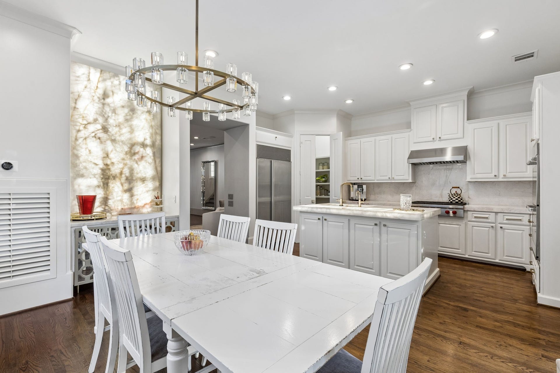 Thoughtfully designed for everyday living and elegant entertaining, the kitchen spans approximately 11'7" x 17'9" and features a professional-grade suite of Wolf appliances, including a gas cooktop and double ovens, paired with a Sub-Zero refrigerator. Rich quartzite countertops and an illuminated island provide a striking focal point, while the spacious 4'9" x 4' walk-in pantry with custom built-in shelving ensures abundant, organized storage.