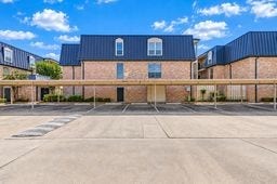 Charming brick townhouse with a sleek dark roof, featuring covered parking and a spacious lot.