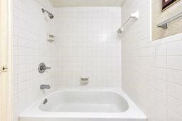 Bright bathroom featuring a clean, white-tiled shower and bathtub, complemented by modern fixtures and a convenient towel rack.