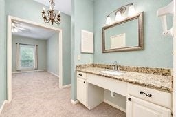 Elegant vanity area with granite countertop and stylish lighting, leading to a cozy carpeted bedroom with a large window for natural light.