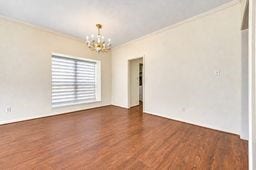 Bright and spacious room featuring elegant wood flooring, a stylish chandelier, and a large window with modern blinds.