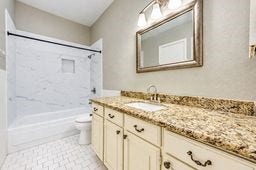 Elegant bathroom featuring a granite countertop, ample cabinetry, and a sleek shower-tub combination with a marble-style surround.