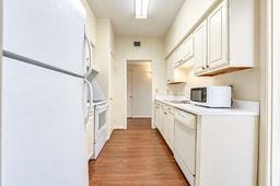 Bright galley kitchen with white cabinetry, modern appliances, and warm wood flooring, offering a clean and functional space.