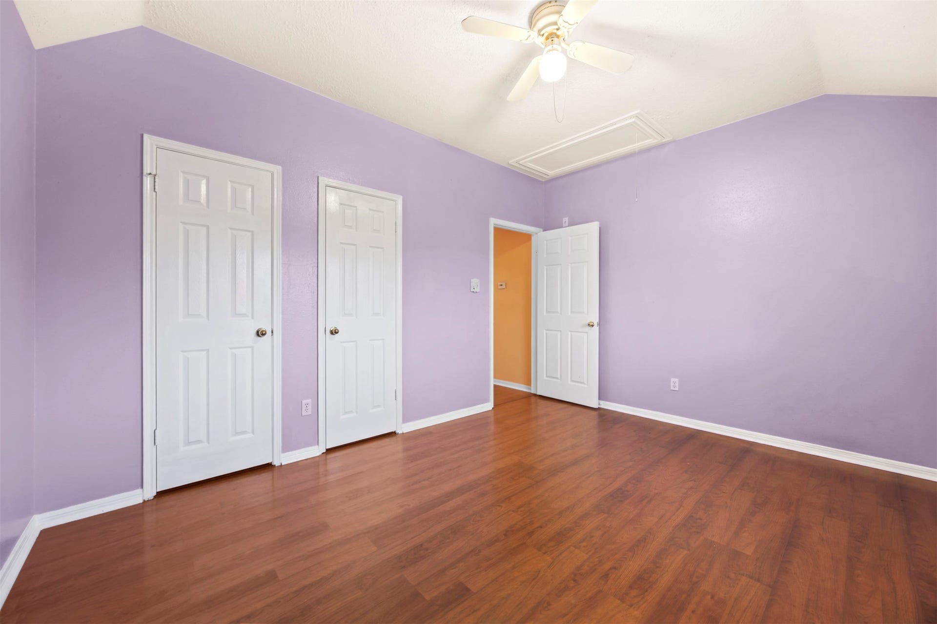 19119 Timber Trace Drive, Humble, TX 77346 Spacious room with warm wood flooring and calming lavender walls, featuring three doors and a ceiling fan for added comfort.