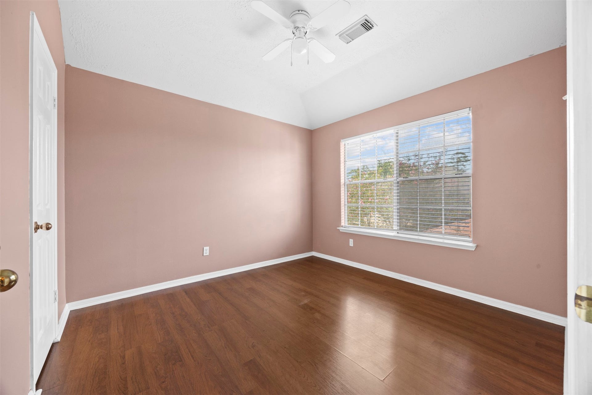 19119 Timber Trace Drive, Humble, TX 77346 Spacious bedroom featuring warm-toned walls, rich hardwood flooring, a ceiling fan, and a large window that fills the space with natural light.