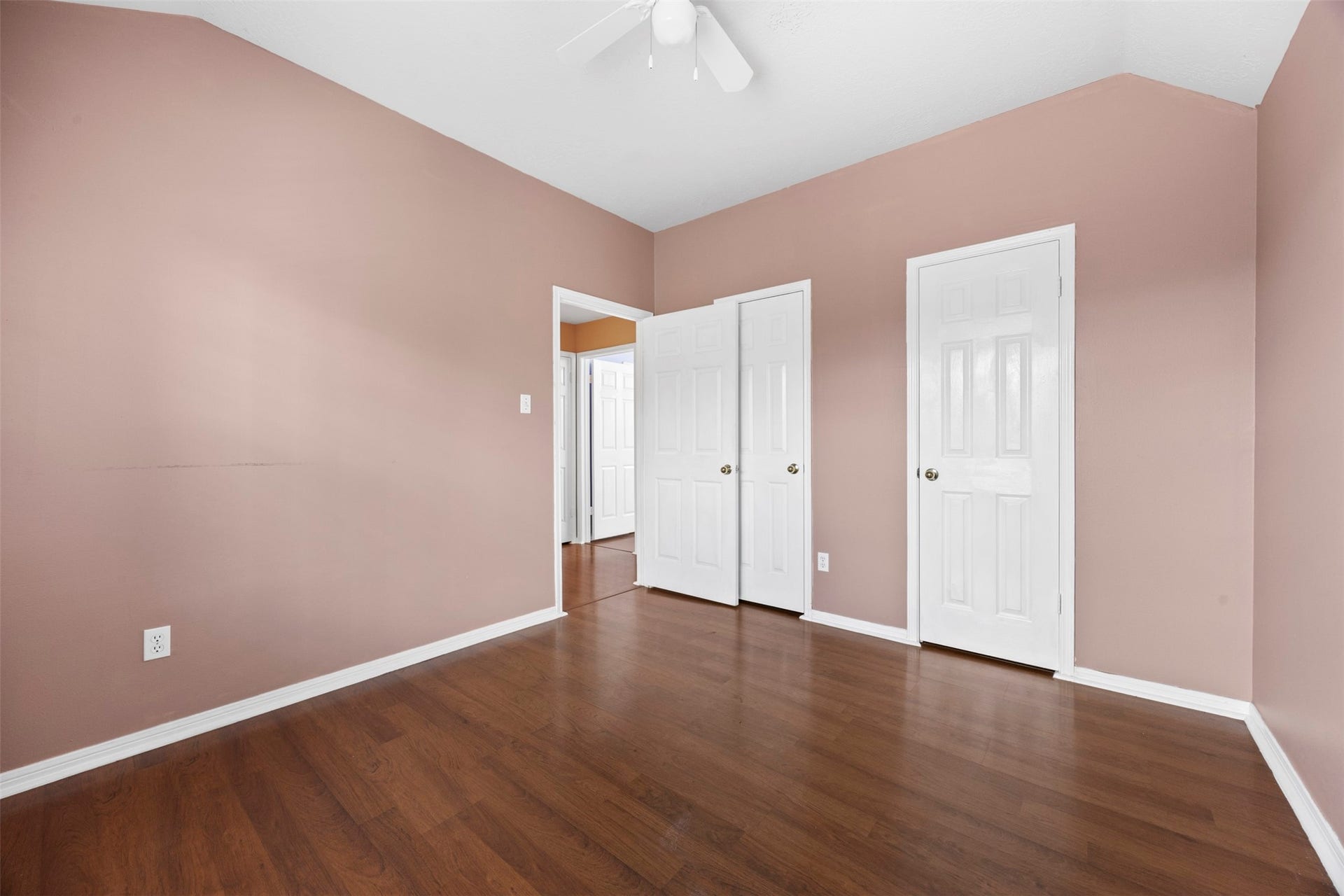 19119 Timber Trace Drive, Humble, TX 77346 Spacious bedroom with warm, neutral walls and rich wood flooring, featuring a ceiling fan and dual white doors for added storage.
