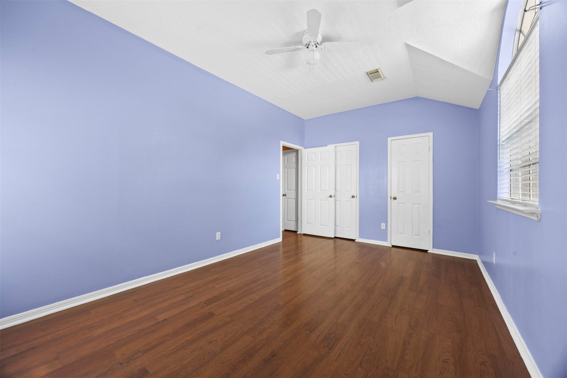 19119 Timber Trace Drive, Humble, TX 77346 Spacious bedroom with calming lavender walls, rich hardwood floors, and ample natural light from large windows.