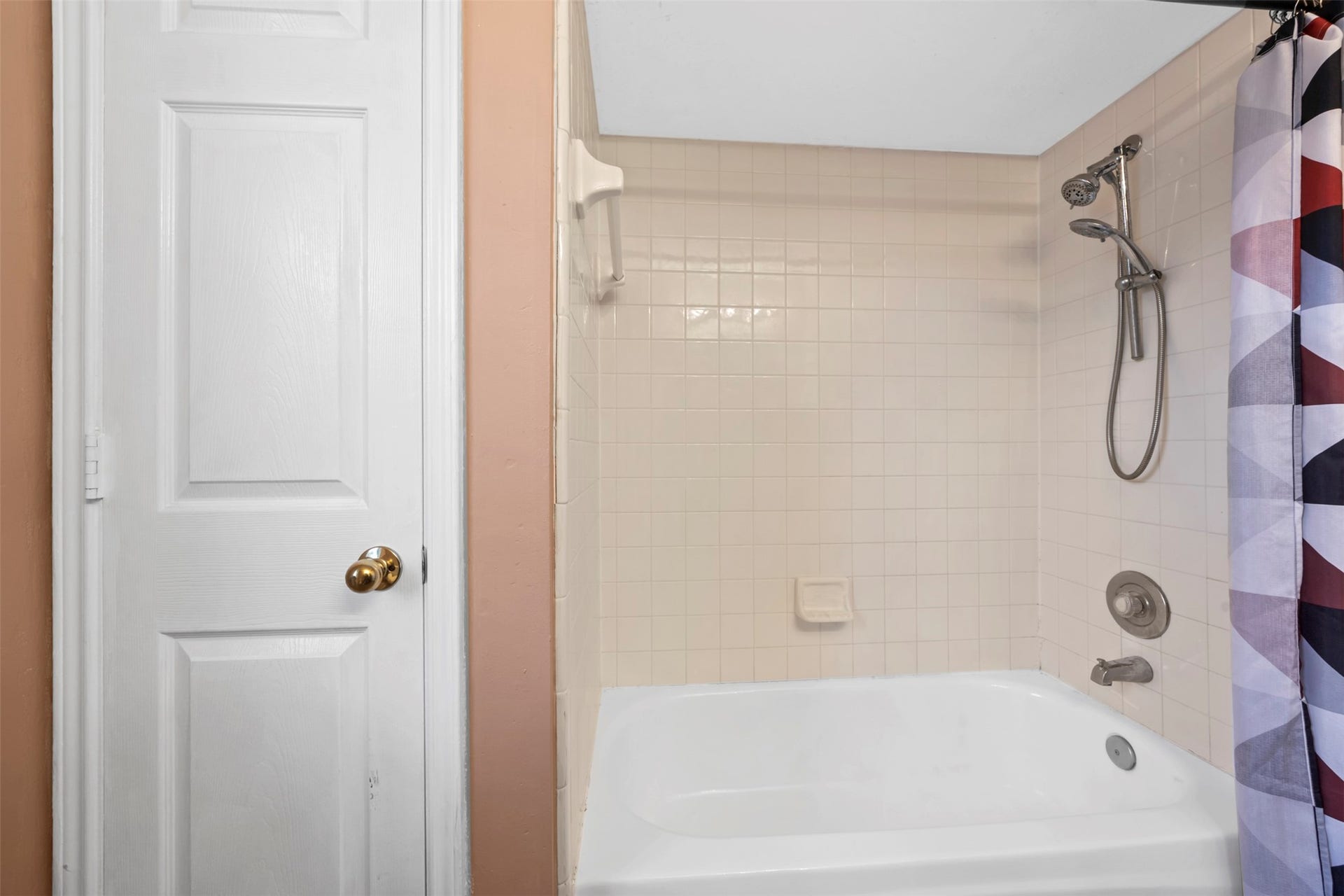 19119 Timber Trace Drive, Humble, TX 77346 Charming bathroom with a classic white tub and shower combination, complemented by a geometric shower curtain and light-colored tile walls.