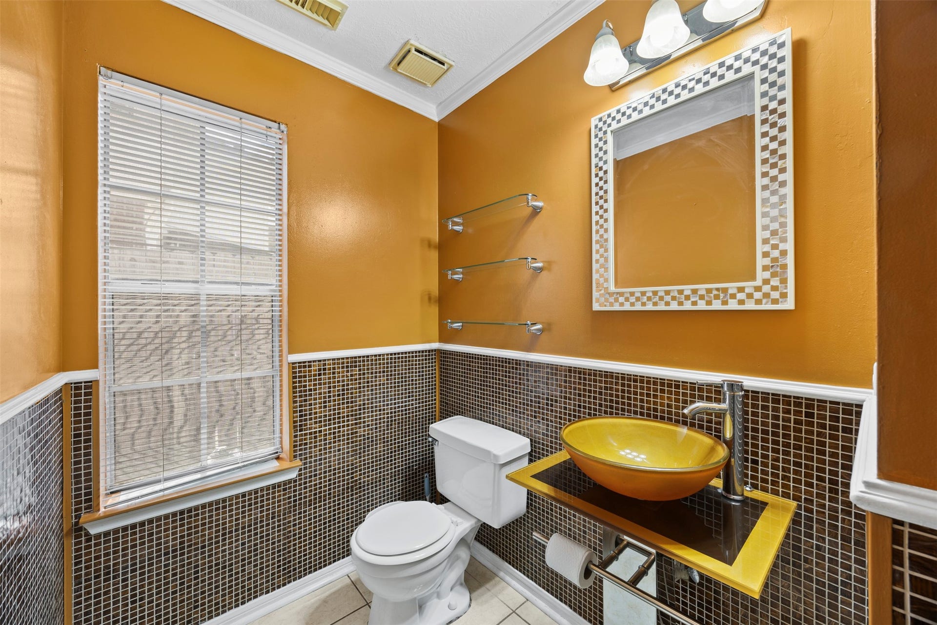 19119 Timber Trace Drive, Humble, TX 77346 Stylish bathroom featuring warm golden walls, a modern vessel sink, sleek glass shelving, and elegant mosaic tile accents.