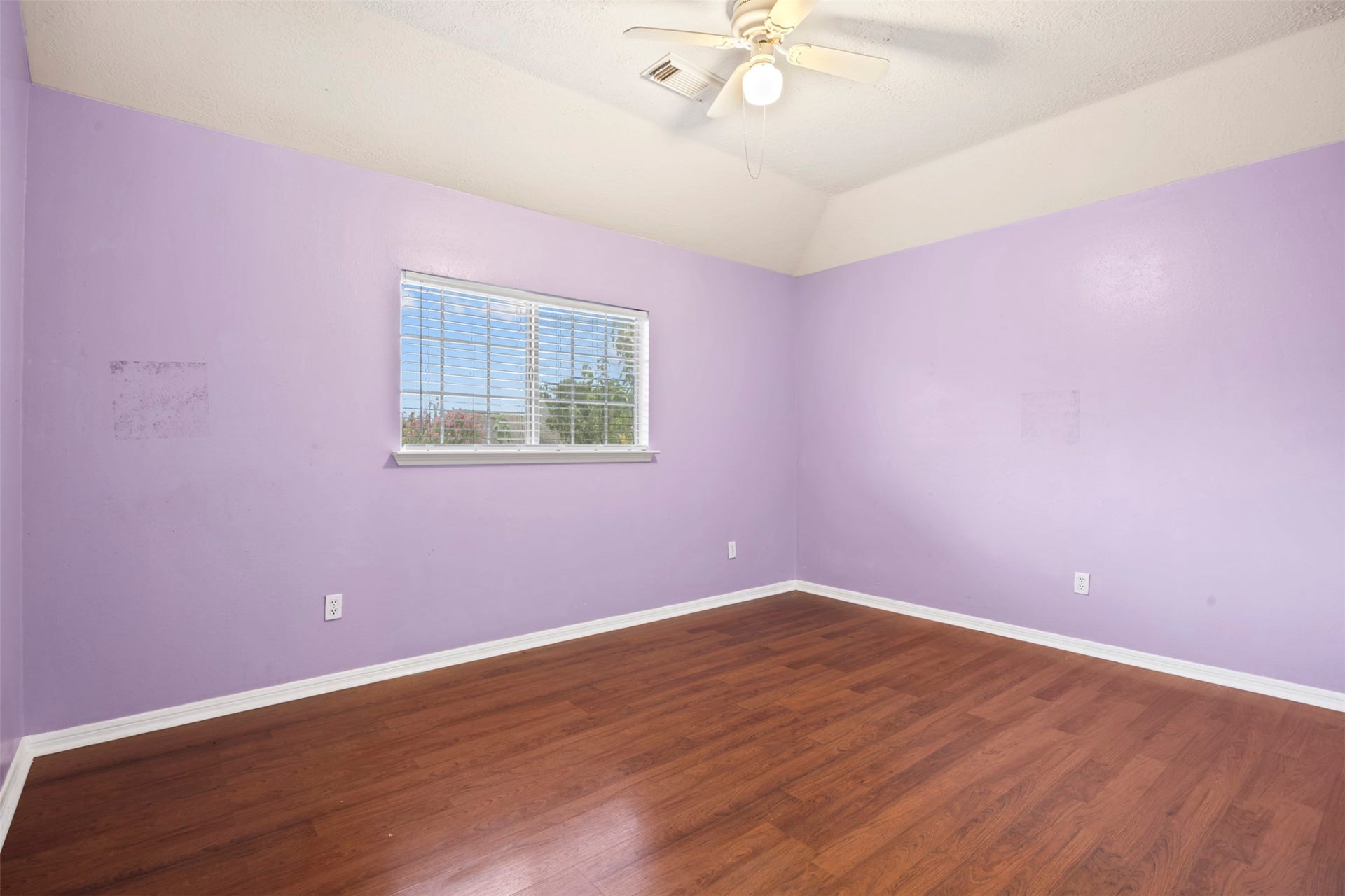 19119 Timber Trace Drive, Humble, TX 77346 Charming bedroom with soft lavender walls, rich wood flooring, and ample natural light from a large window.