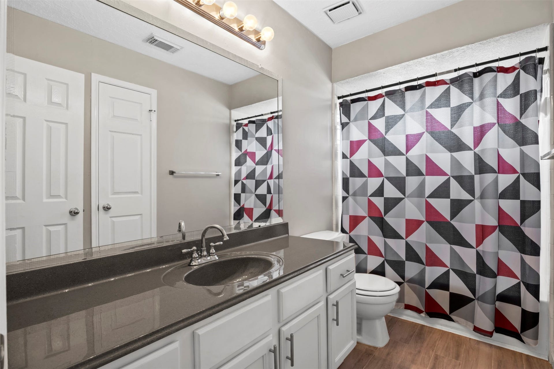19119 Timber Trace Drive, Humble, TX 77346 Modern bathroom featuring a sleek black countertop, stylish geometric shower curtain, and ample cabinet storage.