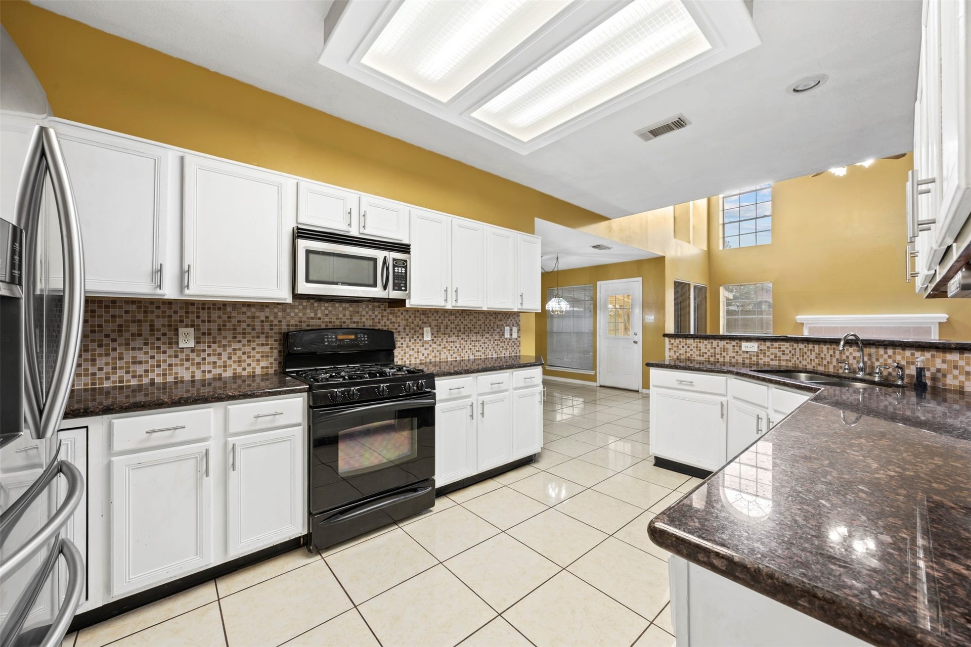 19119 Timber Trace Drive, Humble, TX 77346 Spacious kitchen with sleek white cabinetry, modern appliances, and a stylish tile backsplash, complemented by ample natural light and high ceilings.