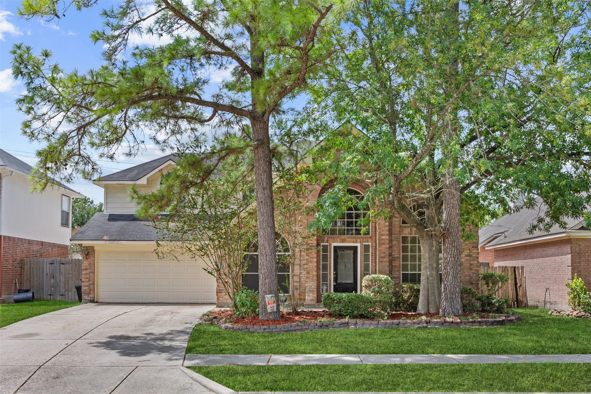 19119 Timber Trace Drive, Humble, TX 77346 Charming brick home with a welcoming front porch, surrounded by mature trees and lush landscaping, featuring a spacious driveway leading to a two-car garage.