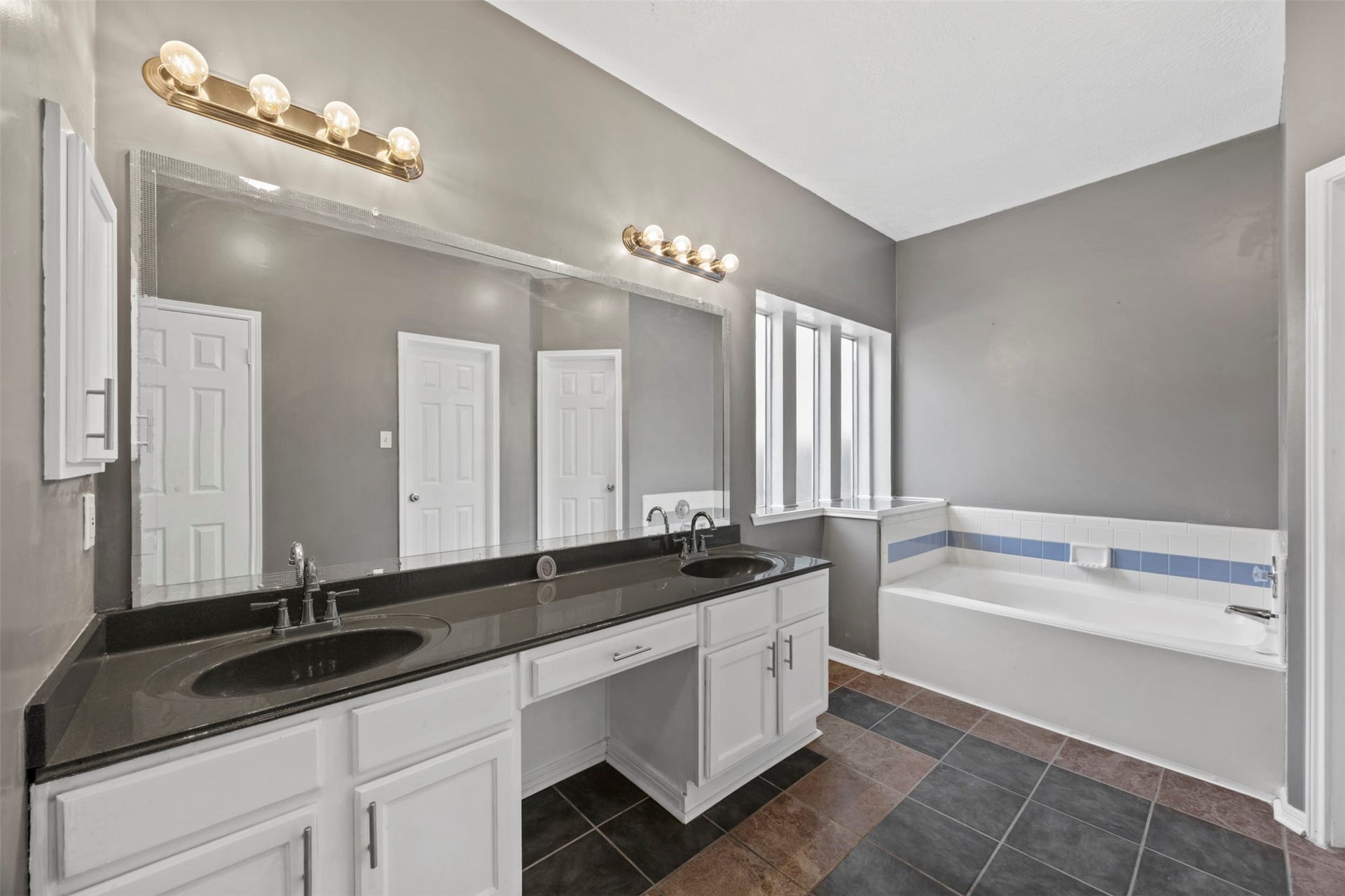 19119 Timber Trace Drive, Humble, TX 77346 Spacious bathroom featuring a double vanity with sleek black countertops, elegant lighting, and a relaxing bathtub with natural light from large windows.