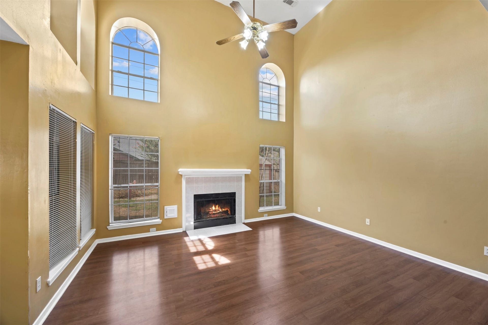 19119 Timber Trace Drive, Humble, TX 77346 A spacious living room featuring soaring ceilings, large arched windows, and a cozy fireplace, offering abundant natural light and warmth.
