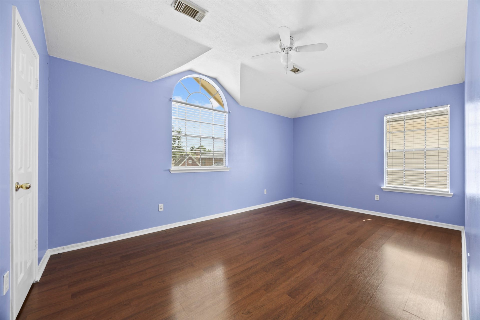 19119 Timber Trace Drive, Humble, TX 77346 Spacious bedroom with vaulted ceiling, featuring soft blue walls and rich hardwood flooring, accented by large windows that fill the room with natural light.