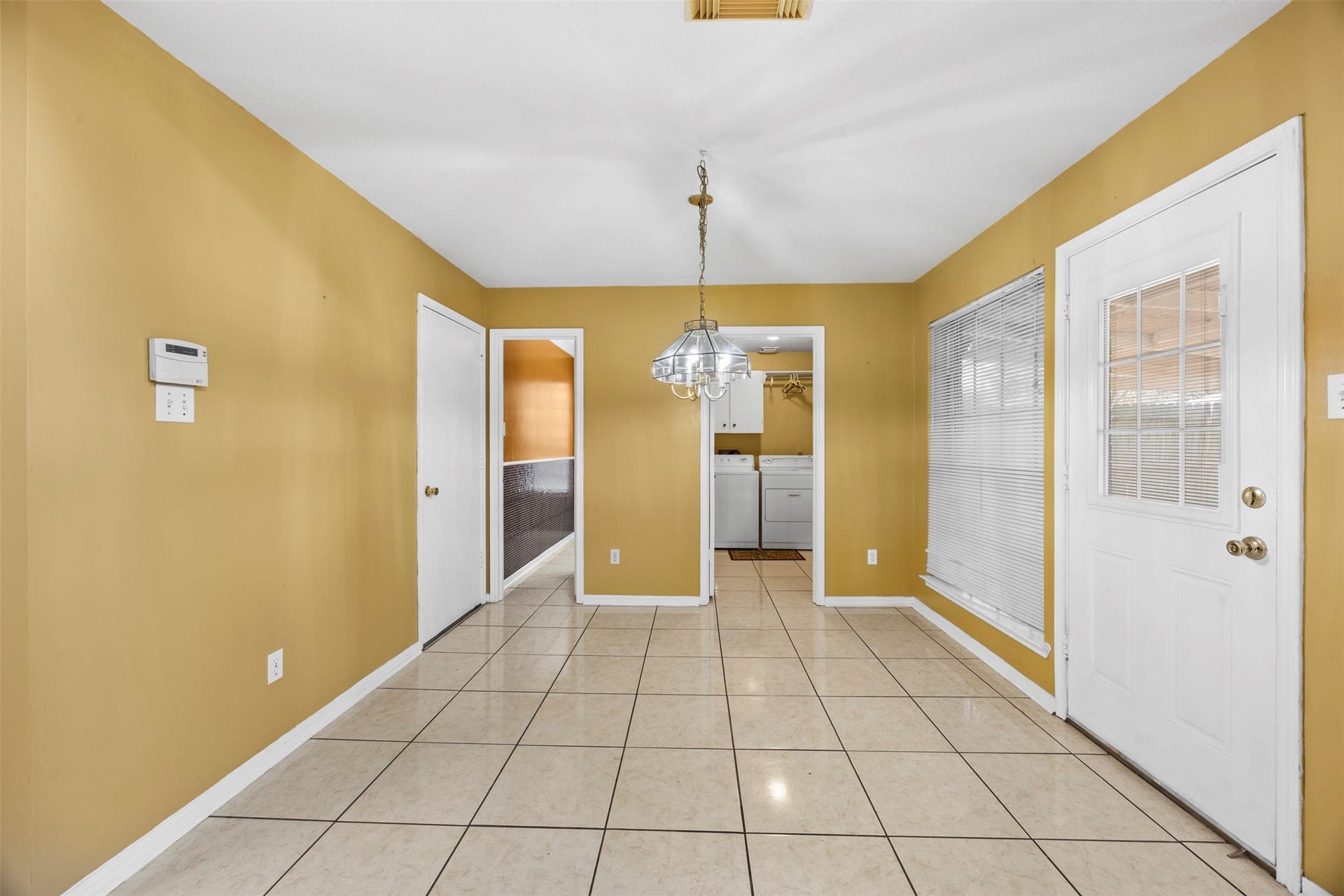 19119 Timber Trace Drive, Humble, TX 77346 Bright dining area with tiled flooring, warm yellow walls, and a stylish chandelier, leading to a laundry room and outdoor access through a glass-paneled door.