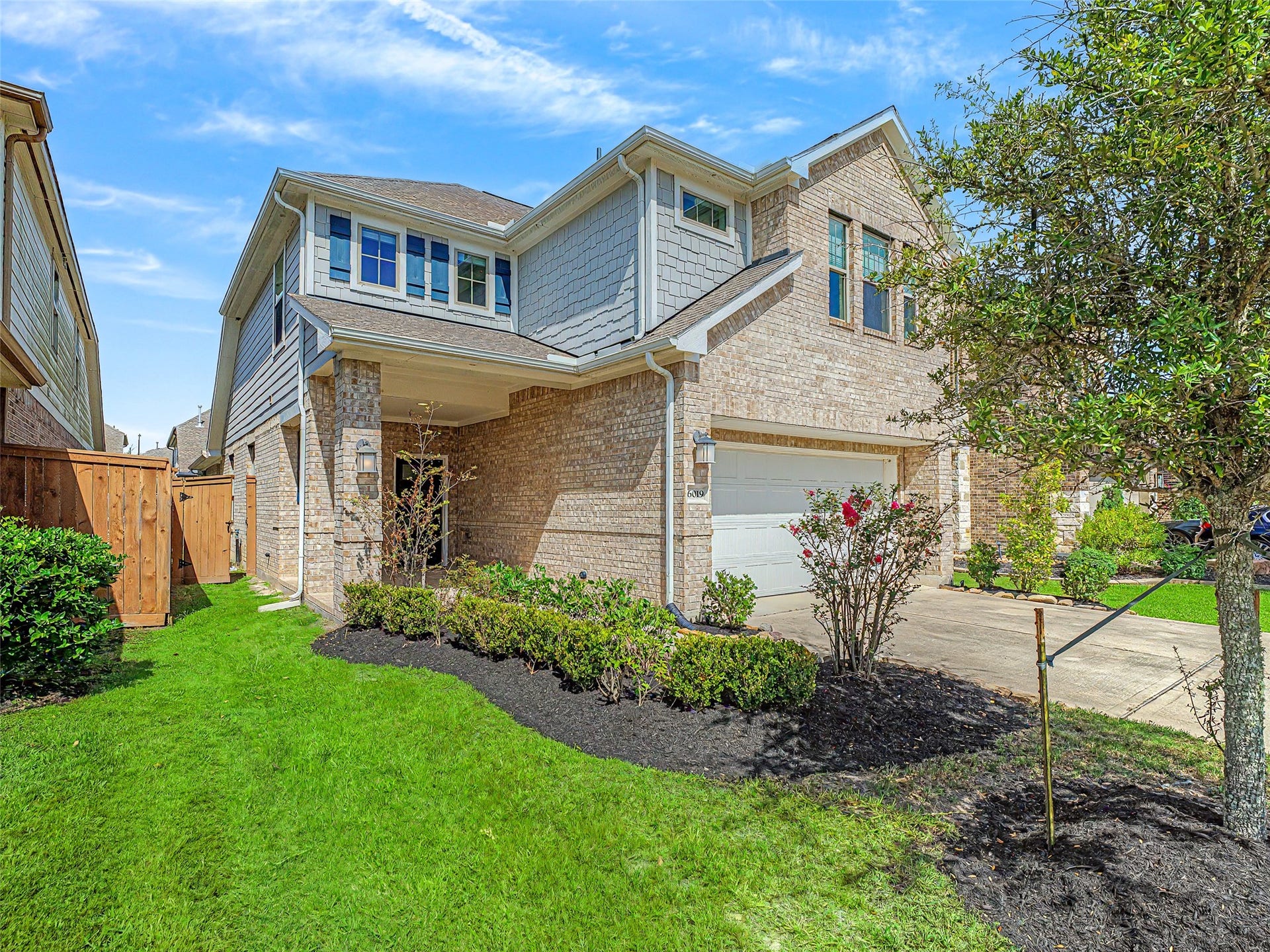 6019 Dovetail Cliff Court, Katy, TX 77493 Featuring a classic combination of light brick masonry and accent siding, this residence instantly captures attention with its lush lawn, established trees, fresh mulch beds, and welcoming covered entryway.