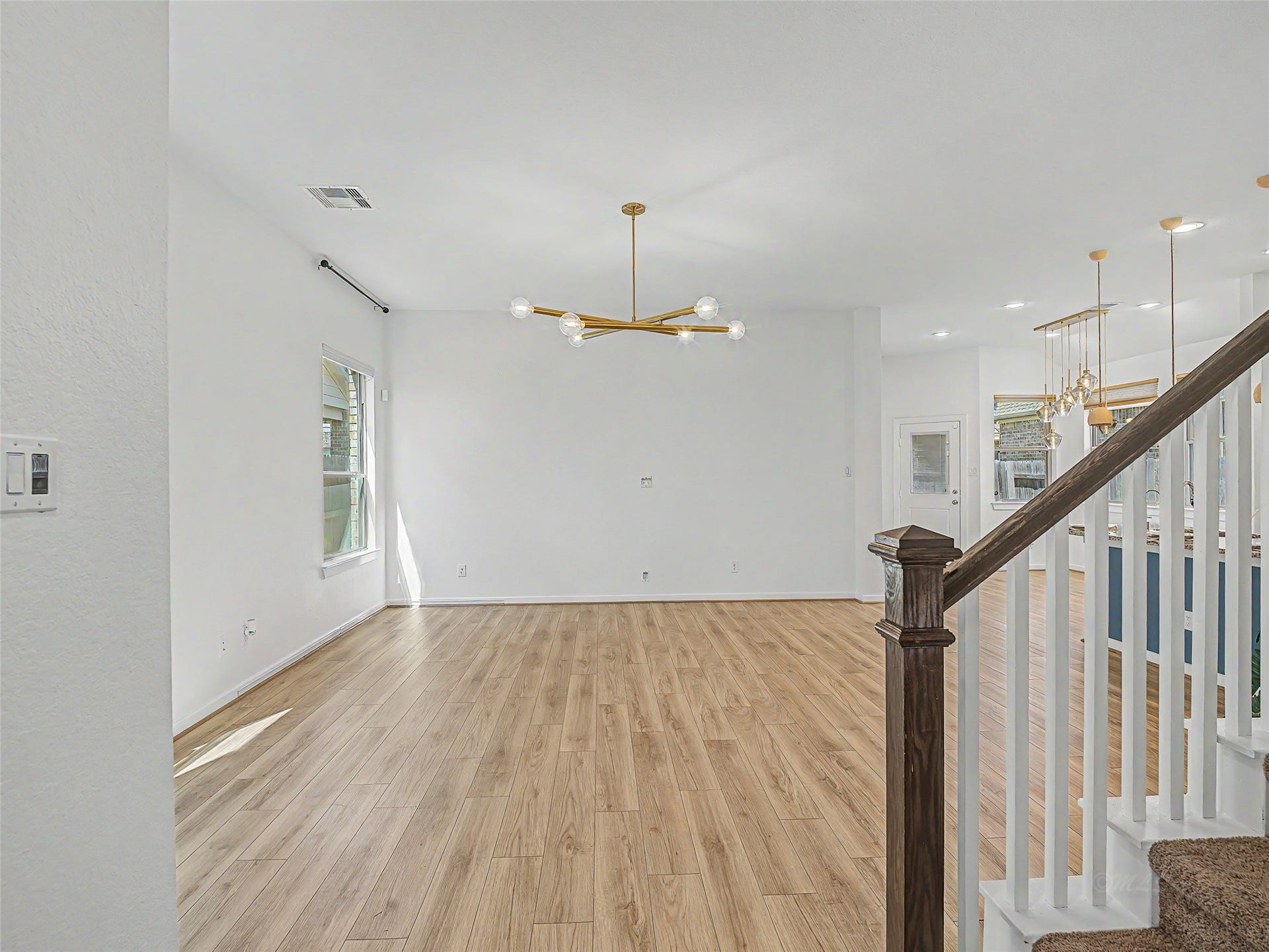 6019 Dovetail Cliff Court, Katy, TX 77493 The central living area is defined by its clean, white walls and abundant natural light from a window on the left wall, which overlooks the exterior. Above, a striking modern sputnik-style chandelier in a brass or gold finish serves as a focal point. Recessed ceiling lights further illuminate the space.