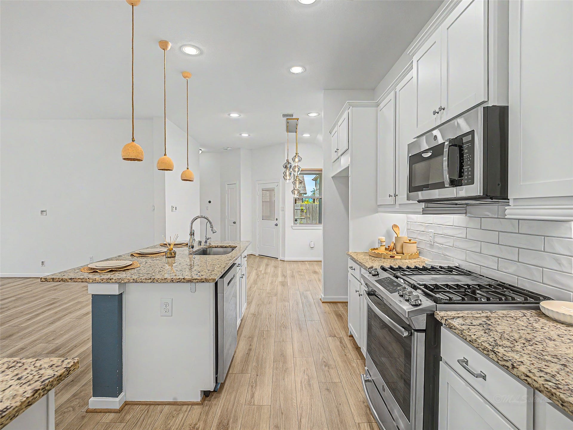 6019 Dovetail Cliff Court, Katy, TX 77493 Suspended above the island, three ceramic pendant light fixtures serve as a decorative focal point, complemented by recessed ceiling lights throughout.