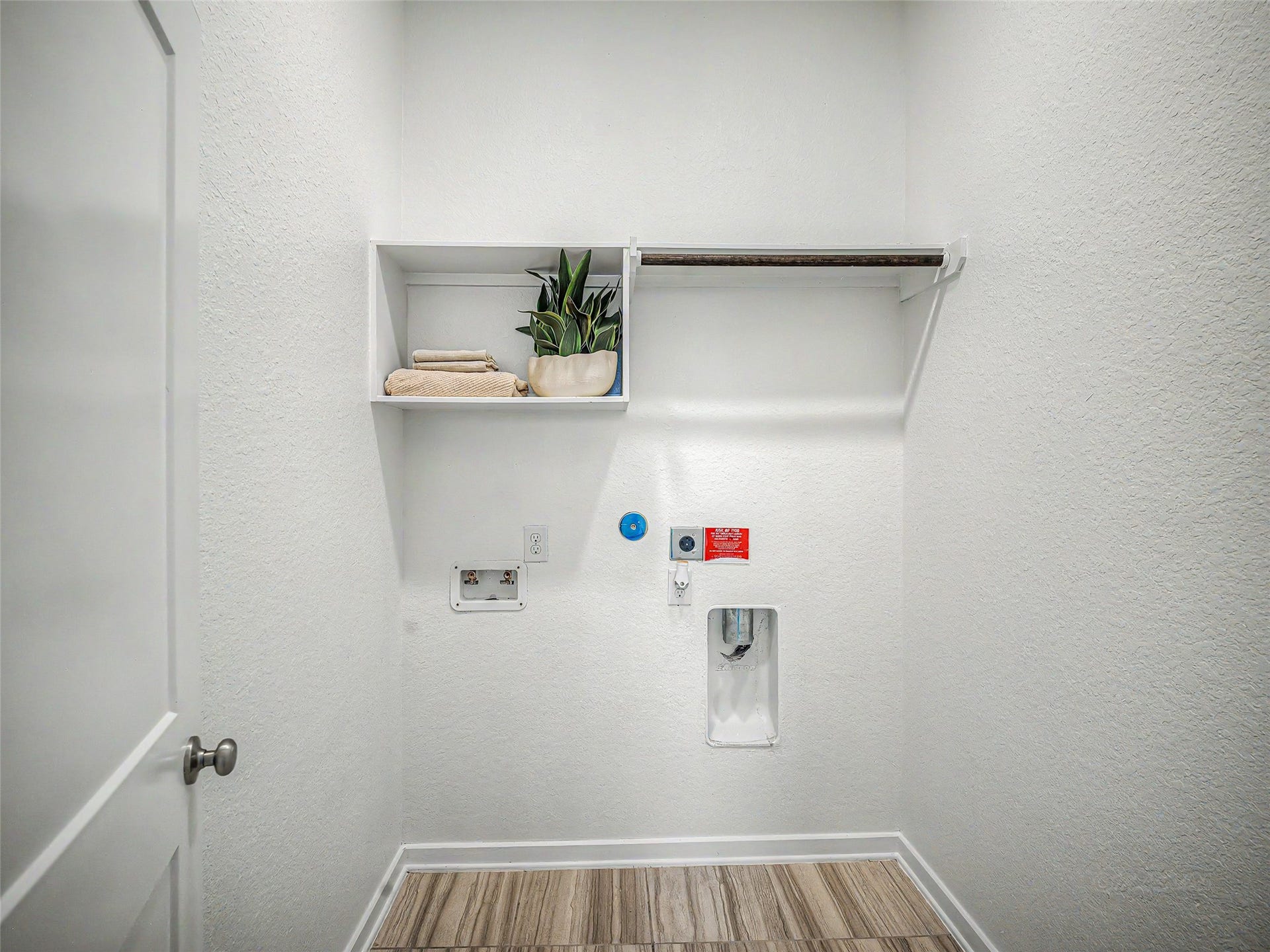 6019 Dovetail Cliff Court, Katy, TX 77493 The room features full washer and dryer hookups with recessed utility connections, plus custom overhead shelving and an integrated hanging rod for easy storage and organization.