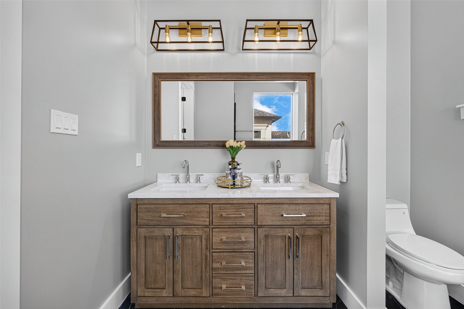 Spacious dual vanity featuring custom wood cabinetry, marble counters, dual sinks, and stylish overhead pendant lights.
