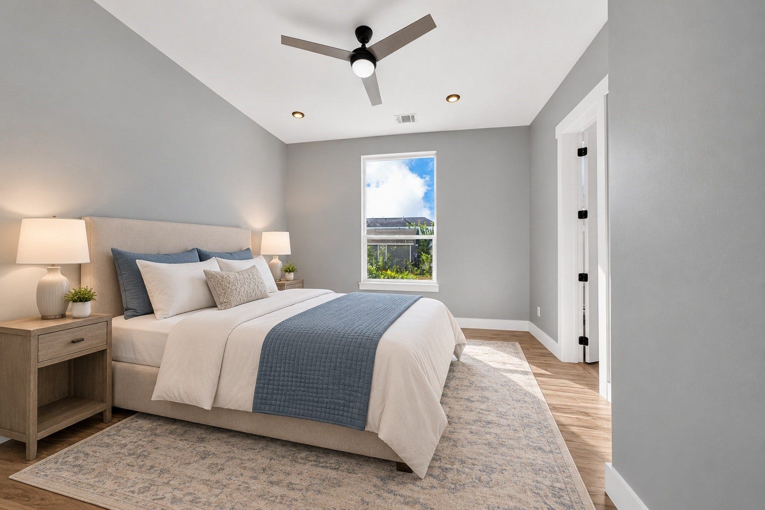 Welcoming first-floor guest bedroom with stylish wood-finish flooring, crisp white trim, a sleek ceiling fan, and a bright window overlooking the outdoors. (virtual staged)