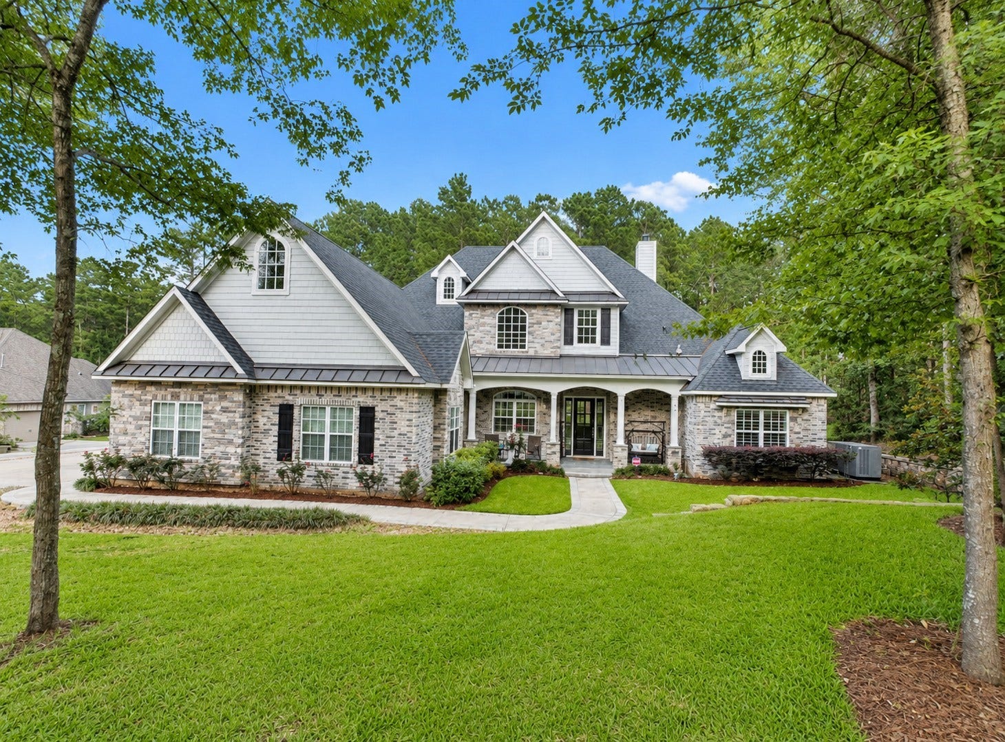 9634 Longmire Creek Way, Conroe, TX 77304 Stunning 1.5-story home with charming dormer windows and elegant stone accents, nestled in a lush, landscaped setting.