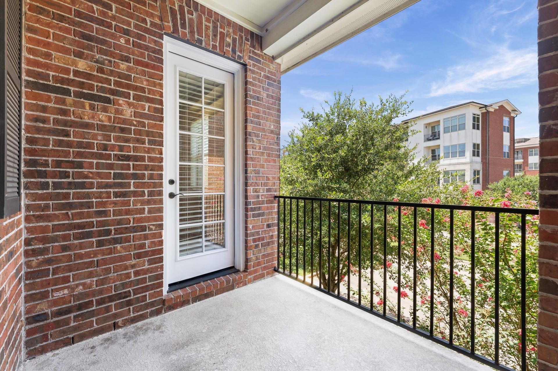 118 Stadium Drive, Sugar Land, TX 77498 Charming balcony with a classic brick exterior and French door entry, offering a serene view of lush greenery and nearby buildings.