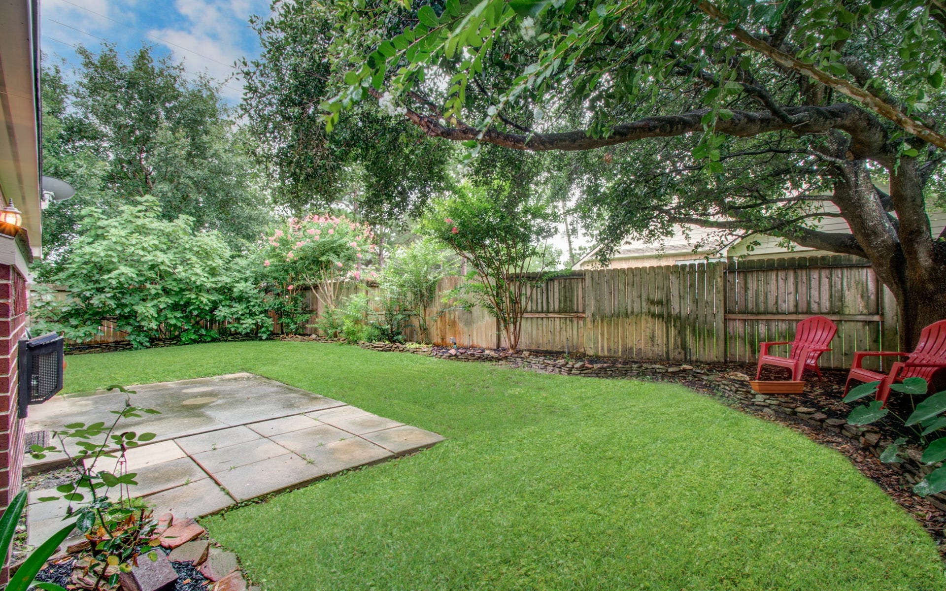14403 Red Tailed Hawk Lane, Houston, TX 77044 Tranquil backyard oasis with lush greenery, a spacious patio, and cozy seating under the shade of mature trees.