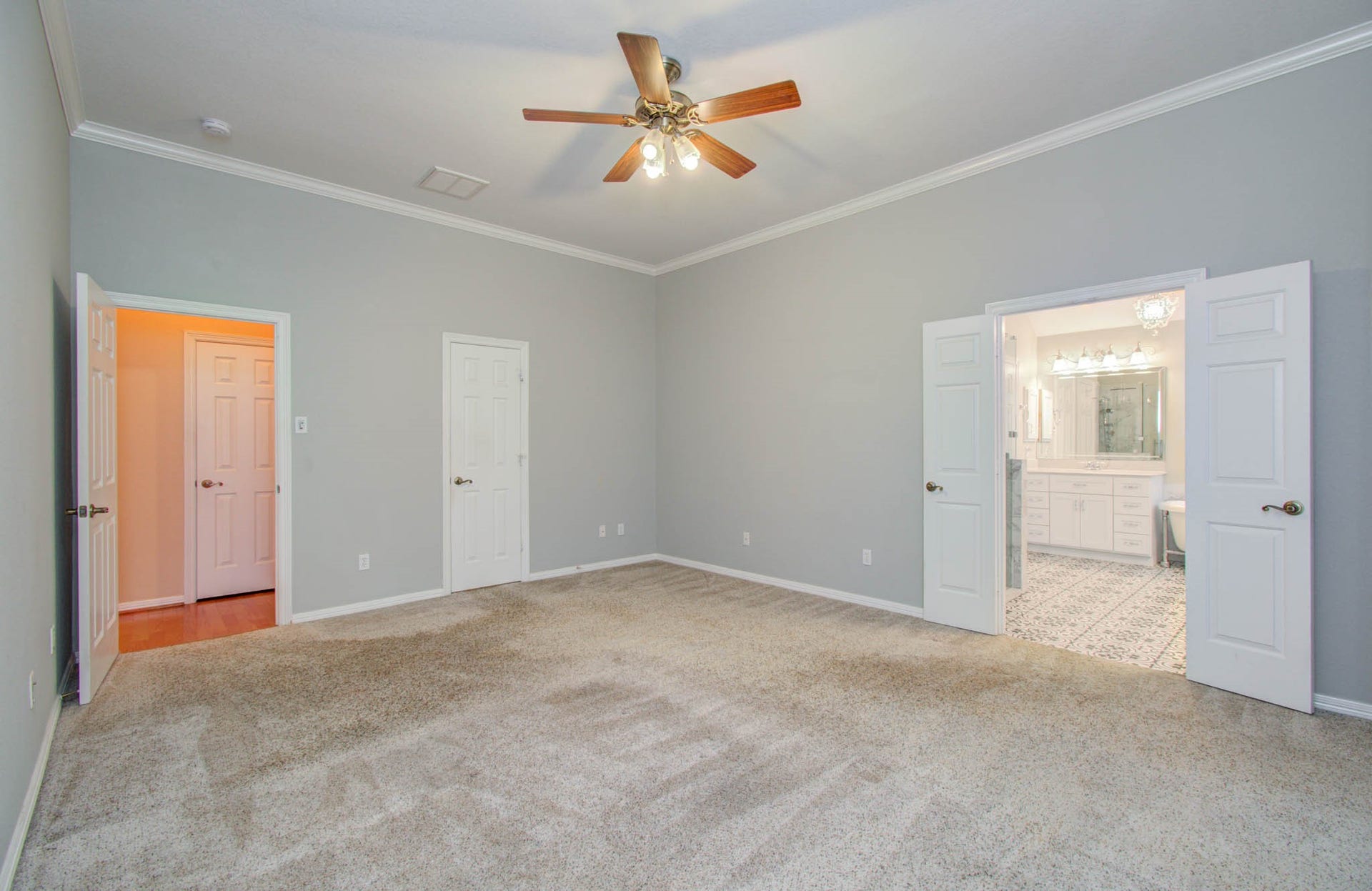 14403 Red Tailed Hawk Lane, Houston, TX 77044 Spacious bedroom with soft carpeting, elegant crown molding, and ceiling fan, leading to a luxurious en-suite bathroom through double doors.