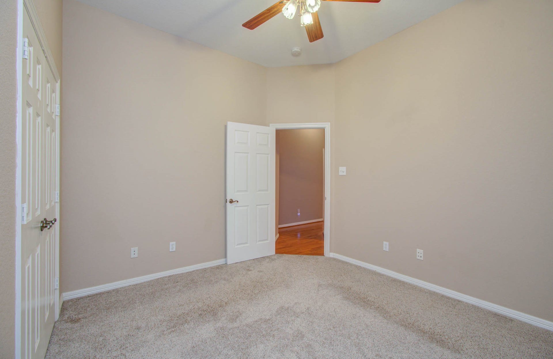 14403 Red Tailed Hawk Lane, Houston, TX 77044 Bright bedroom with soft carpet, neutral walls, and a ceiling fan, featuring ample closet space and a doorway leading to hardwood floors.