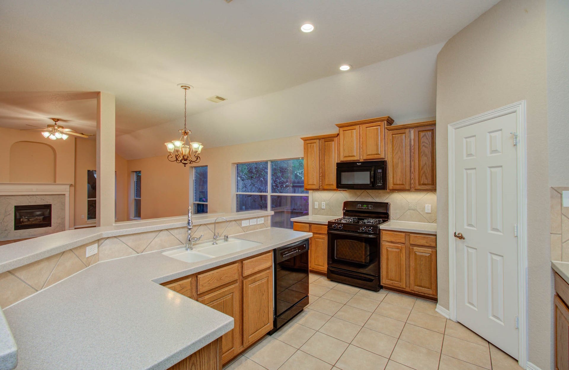 14403 Red Tailed Hawk Lane, Houston, TX 77044 Spacious kitchen with warm wood cabinetry, sleek black appliances, and a convenient breakfast bar, seamlessly connecting to a cozy living area with a fireplace.