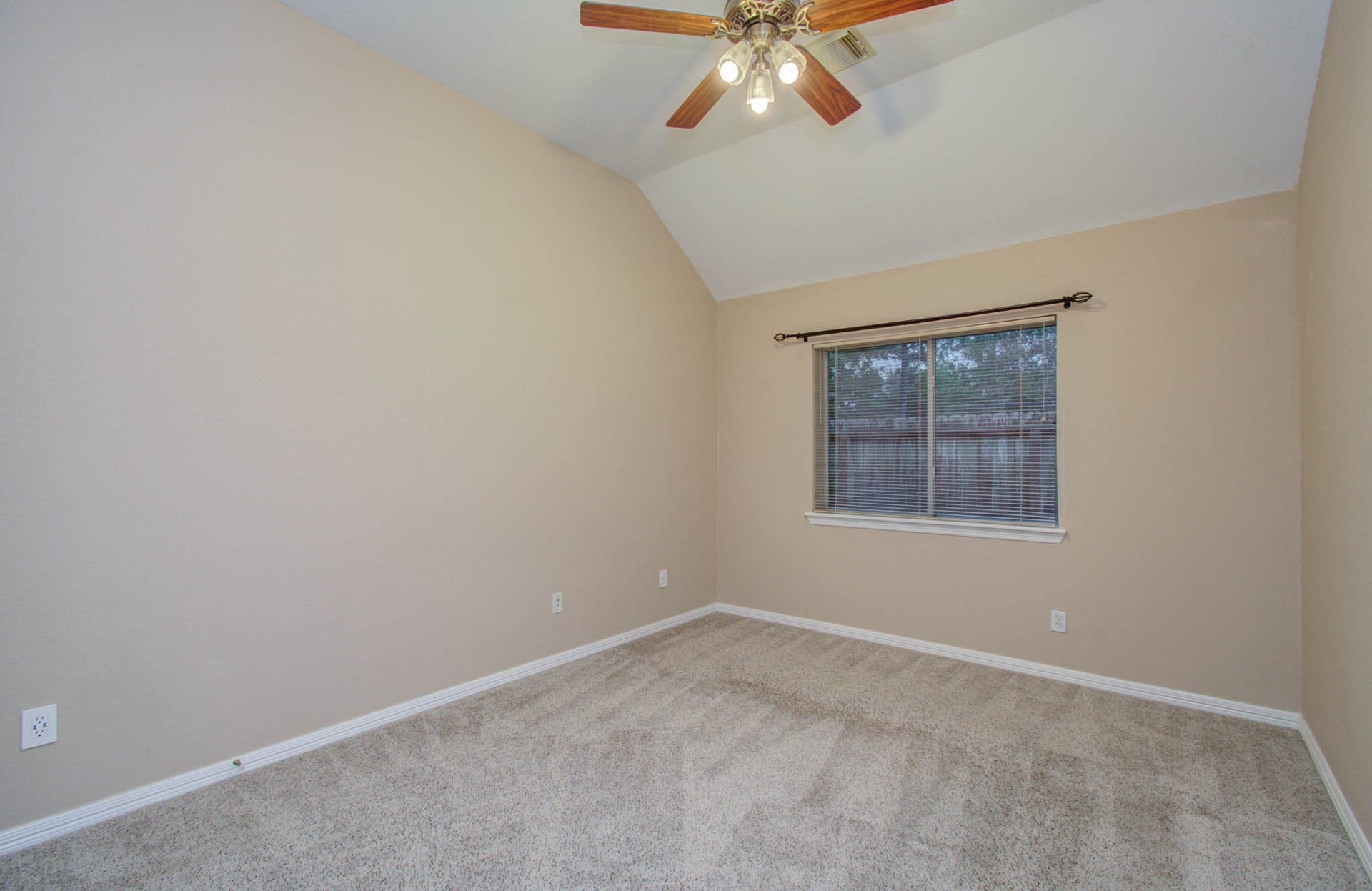 14403 Red Tailed Hawk Lane, Houston, TX 77044 Cozy bedroom with soft carpeting, neutral walls, and a vaulted ceiling featuring a stylish ceiling fan. Natural light pours in through the window, creating a warm and inviting atmosphere.