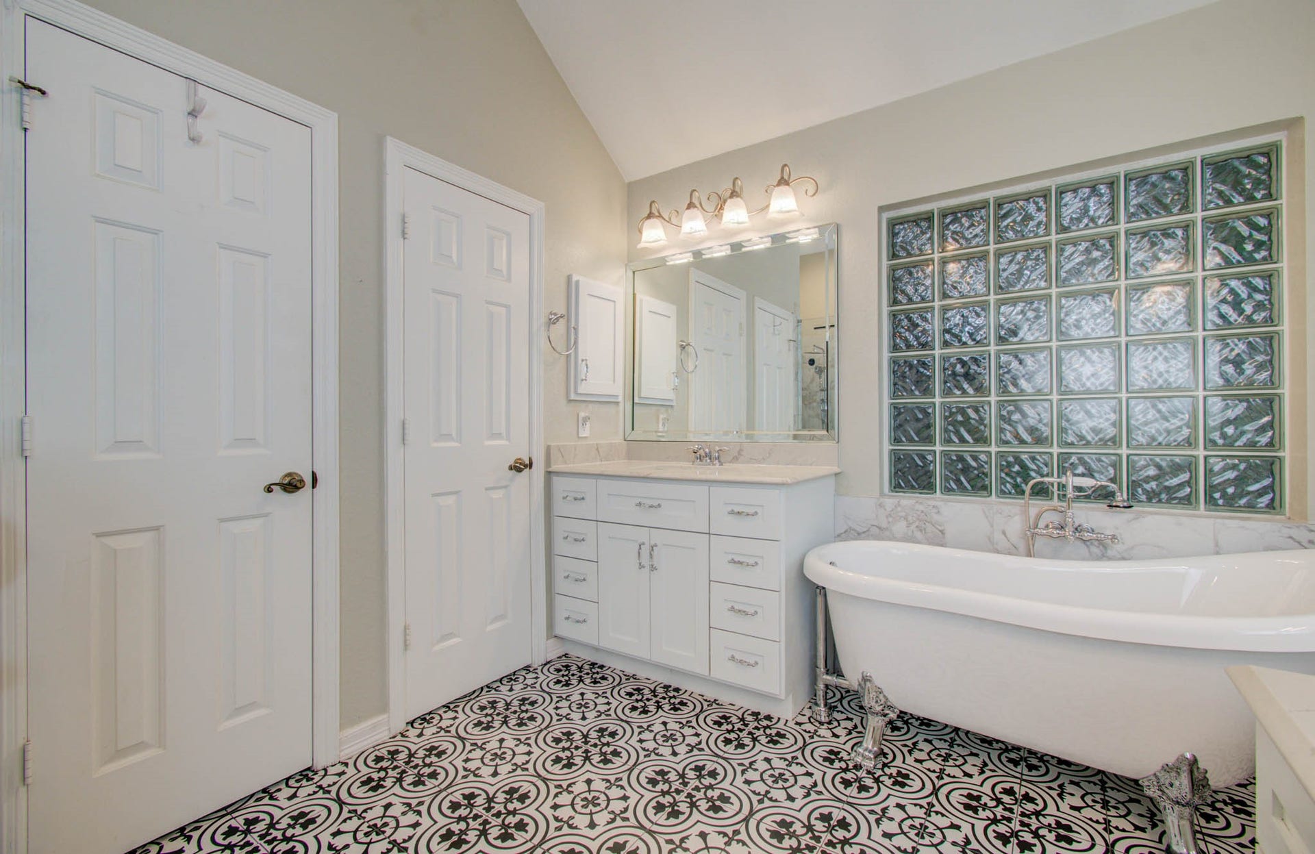 14403 Red Tailed Hawk Lane, Houston, TX 77044 Elegant bathroom featuring a classic clawfoot tub, stylish patterned floor tiles, and ample natural light through glass block windows.